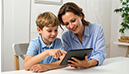 Mutter und Sohn betrachten gemeinsam ein Tablet. Der Junge zeigt auf den Bildschirm, während die Mutter lächelt. (KI-generiertes Bild)