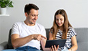 Vater und Tochter betrachten gemeinsam ein Tablet. Der Vater zeigt auf den Bildschirm, während die Tochter lächelt. (KI-generiertes Bild)