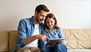 Vater und Tochter betrachten gemeinsam ein Tablet. Der Vater zeigt auf den Bildschirm, während die Tochter lächelt. (KI-generiertes Bild)