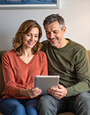 Zwei ältere Menschen schauen gemeinsam auf ein Tablet und lächeln dabei (KI-generiertes Bild)